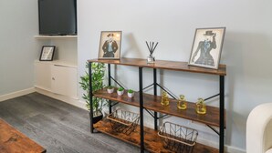 Un soggiorno con una TV, una mensola in legno con fotografie, una pianta e una sedia bianca.