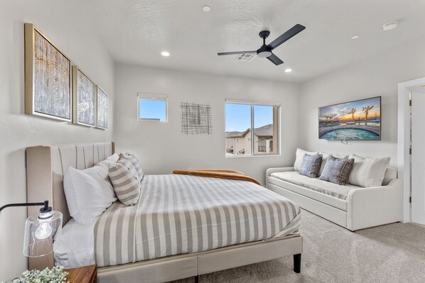 A bedroom with a bed, a sofa, a ceiling fan, and artwork on the walls.