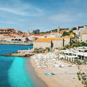 A coastal town with a historic fortification, a sandy beach with sun loungers, and a clear blue sea. - Old Town Centar Dubrovnik Lovely Apartment (Dubrovnik)