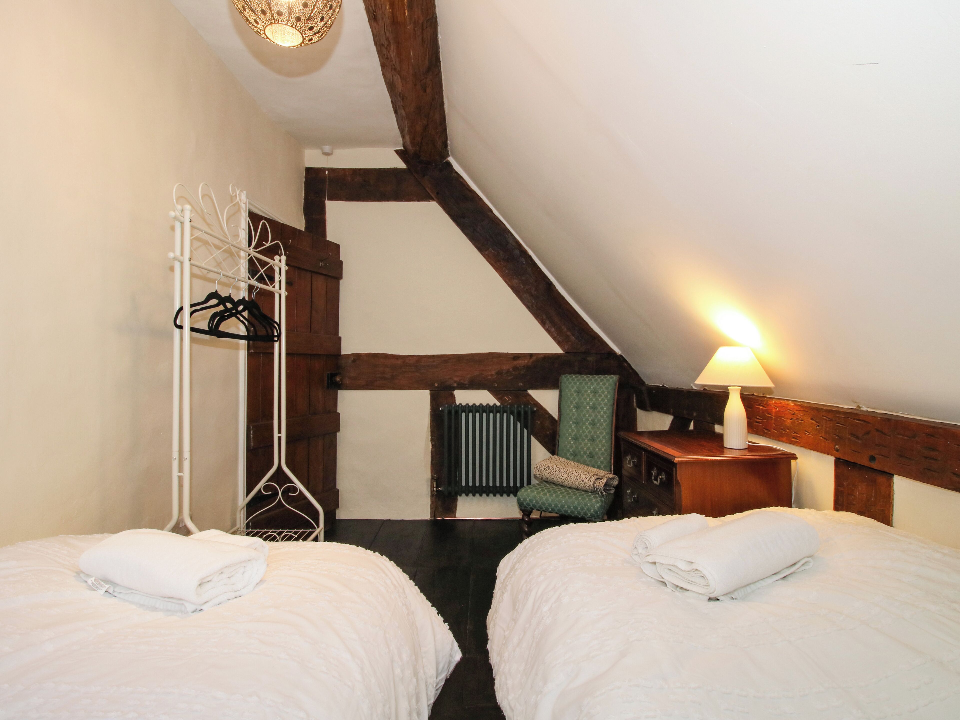 A bedroom with two beds, a radiator, a chair, and a lamp.
