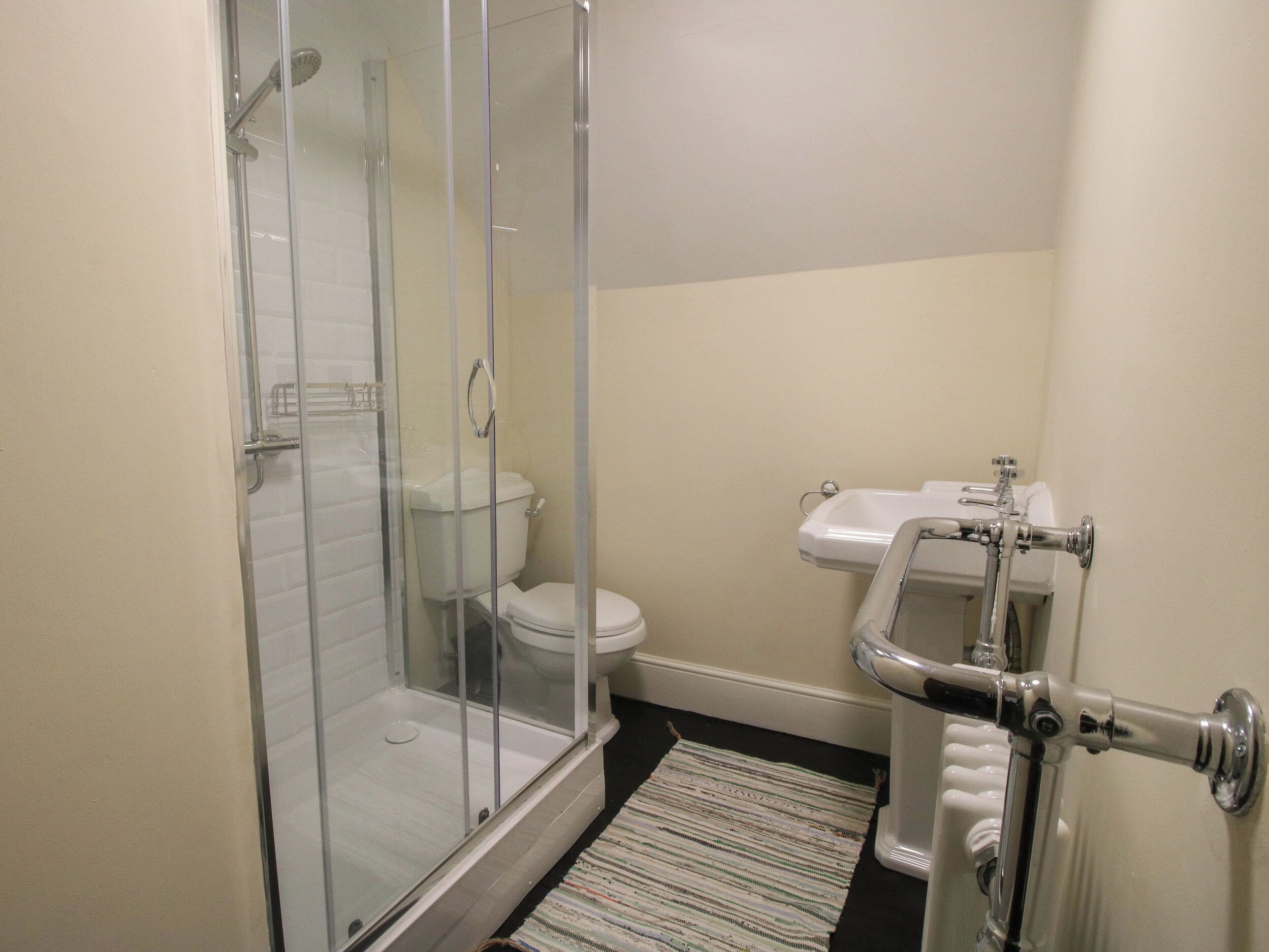 Un baño con ducha envuelta en vidrio, inodoro y lavamanos con grifo cromado.