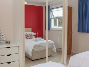 Ein Schlafzimmer mit Bett, Nachttisch, Kommode, einem Fenster mit Vorhängen und einer Heizung.