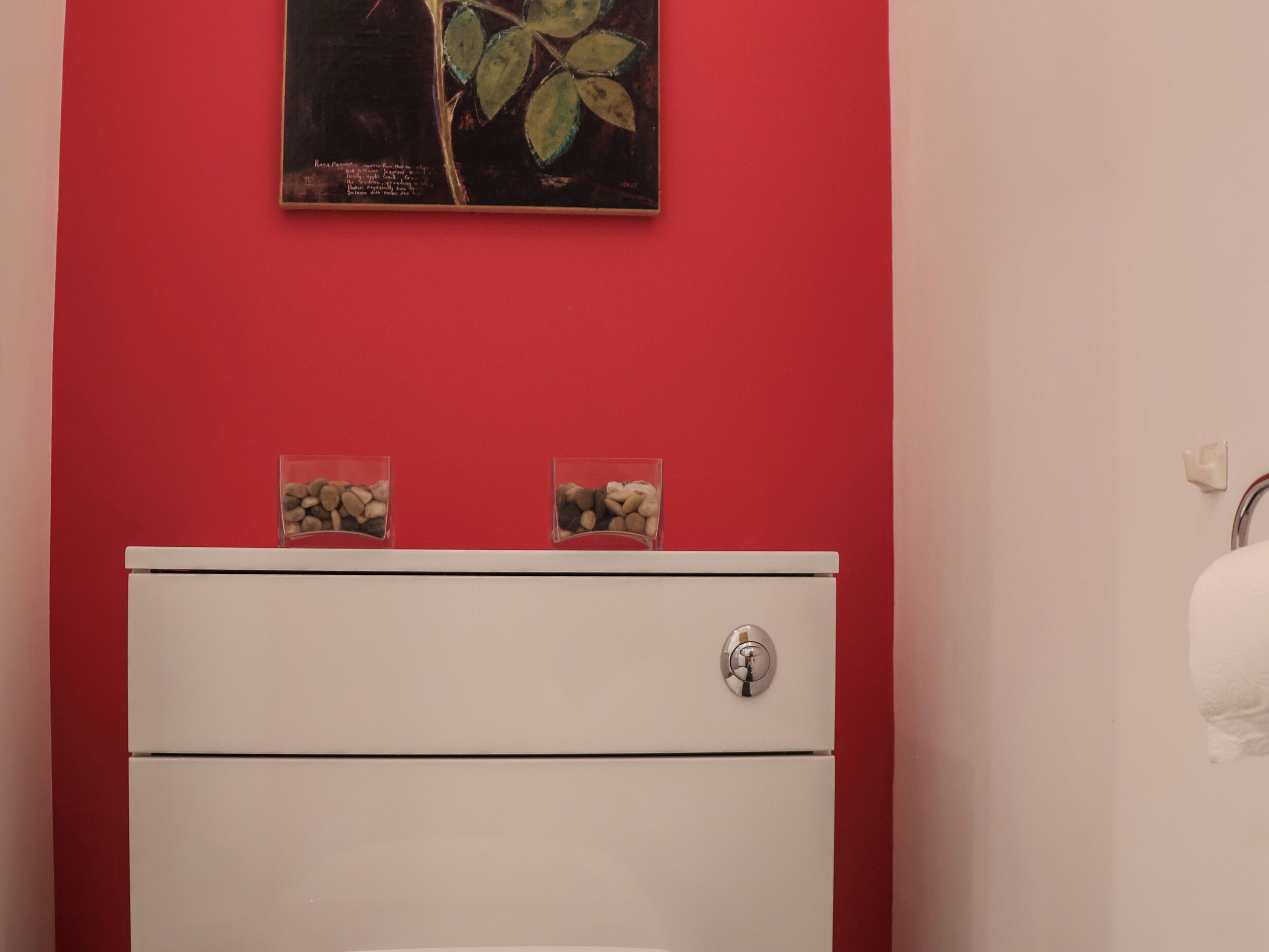 A bathroom with a red wall, a white cabinet, and a painting above the cabinet.