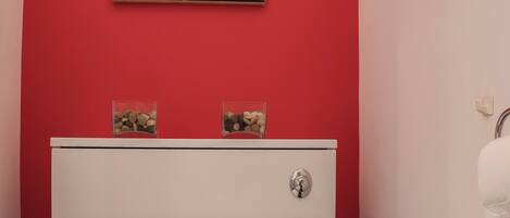 A bathroom with a red wall, a white cabinet, and a painting above the cabinet.