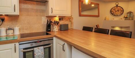 A modern kitchen with white cabinets, a wooden countertop, an oven, a toaster, and a hanging light fixture.