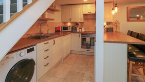 Een compacte keuken met een wasmachine, magnetron, oven en een eethoek met een houten tafel en stoelen.