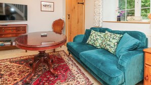 Een woonkamer met een ronde houten tafel, een teal kleurige bank, een rood tapijt met patroon, een houten kast en een televisie aan de muur.