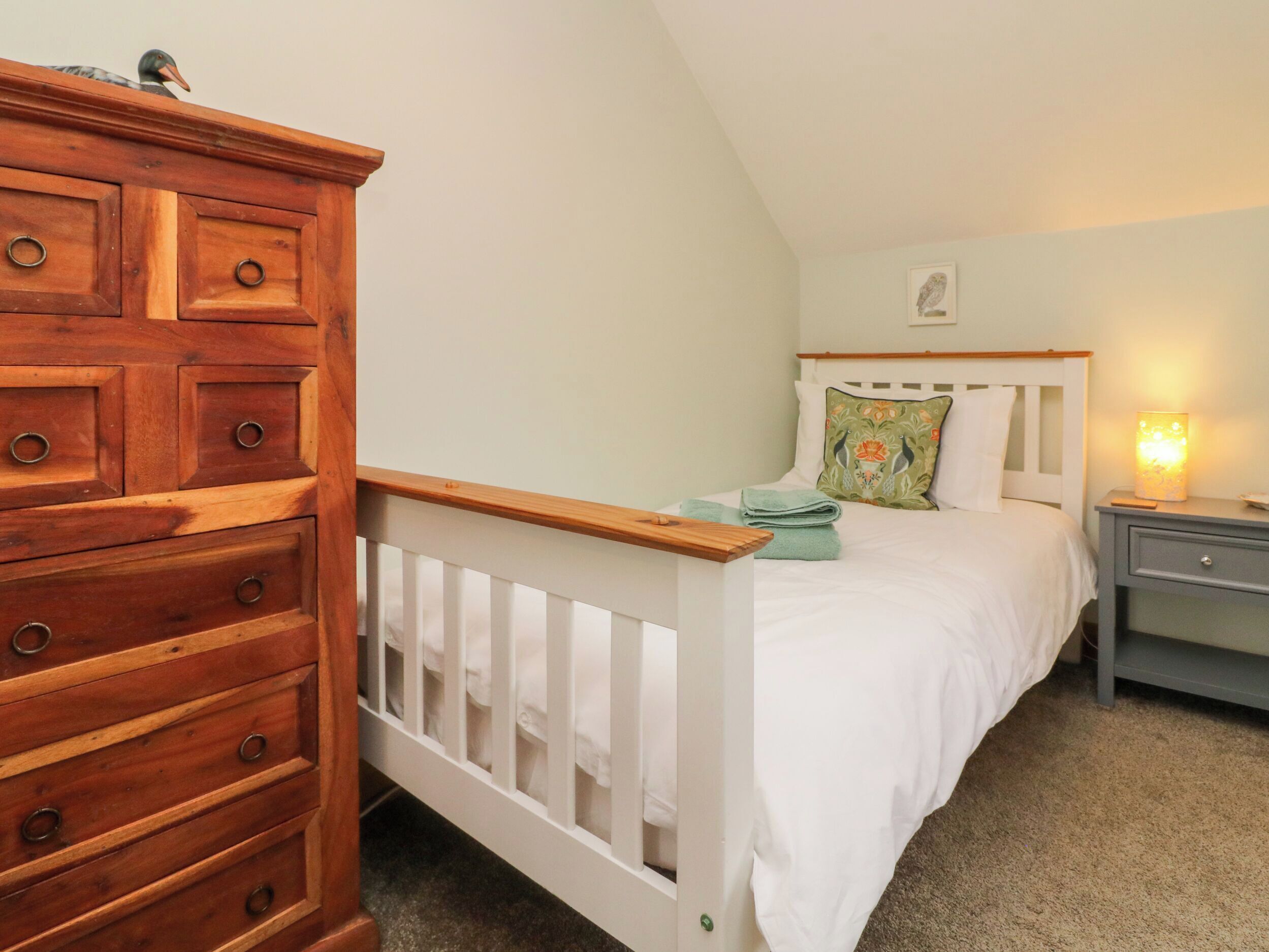Un dormitorio con un aparador de madera, una cuna blanca, una cama con almohada verde y una mesita de noche con lámpara.