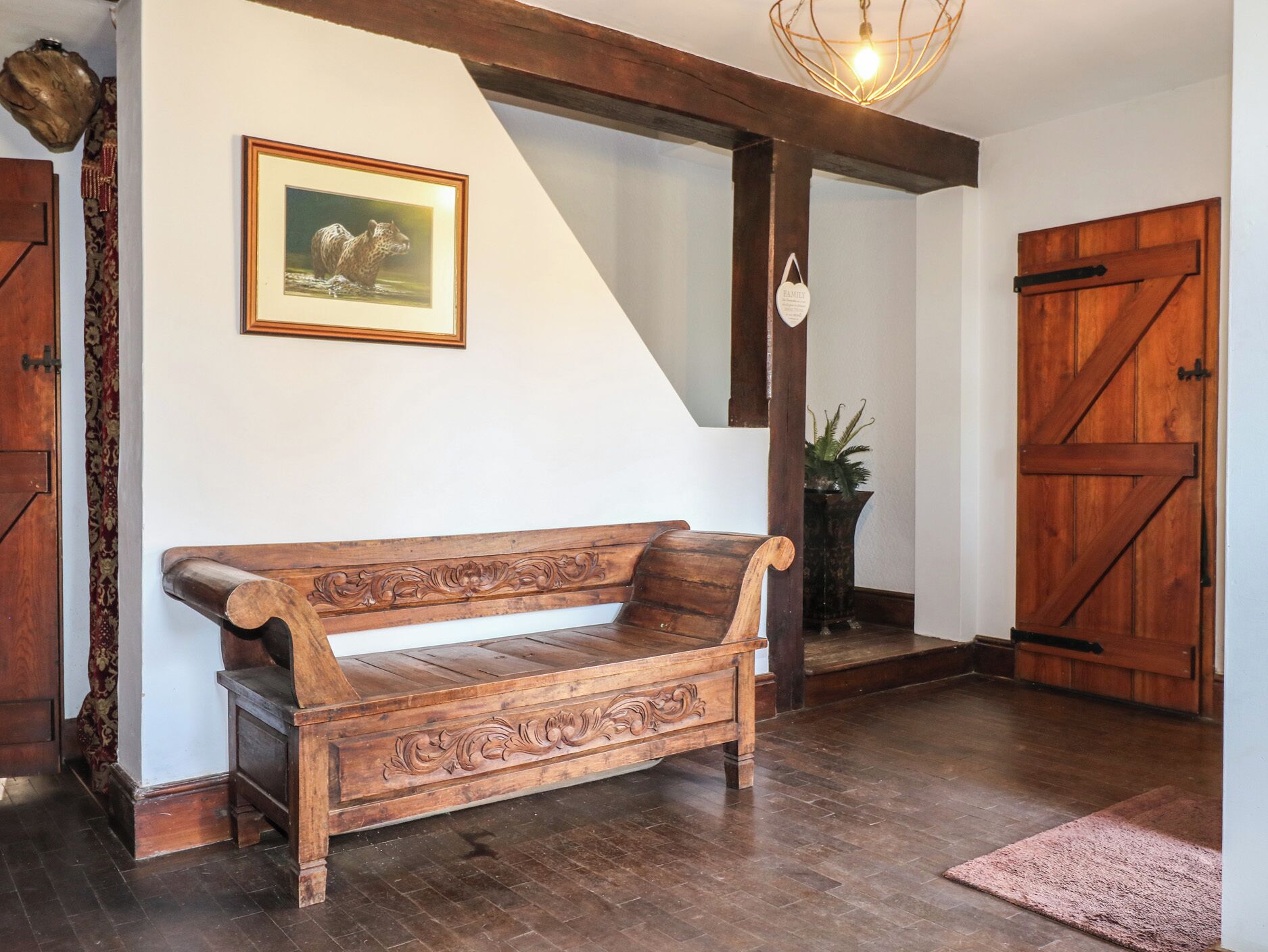 Un banco de madera con tallas intrincadas, un cuadro enmarcado en la pared y una puerta de madera rústica.