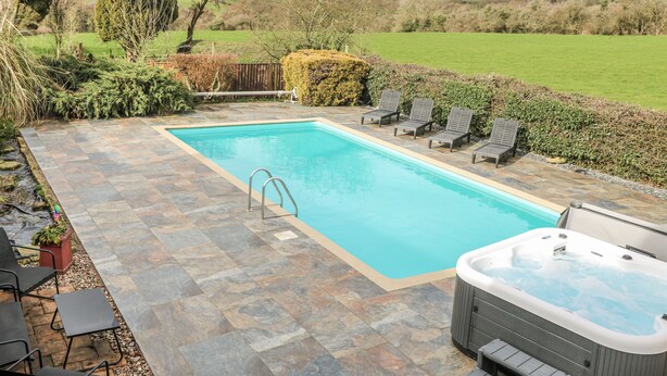 A rectangular swimming pool with a hot tub, surrounded by stone tiles and lounge chairs. - Woodpit Cottage (Nottingham)
