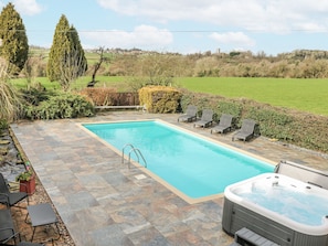 A rectangular swimming pool with a hot tub, surrounded by stone tiles and lounge chairs. - Woodpit Cottage (Nottingham)