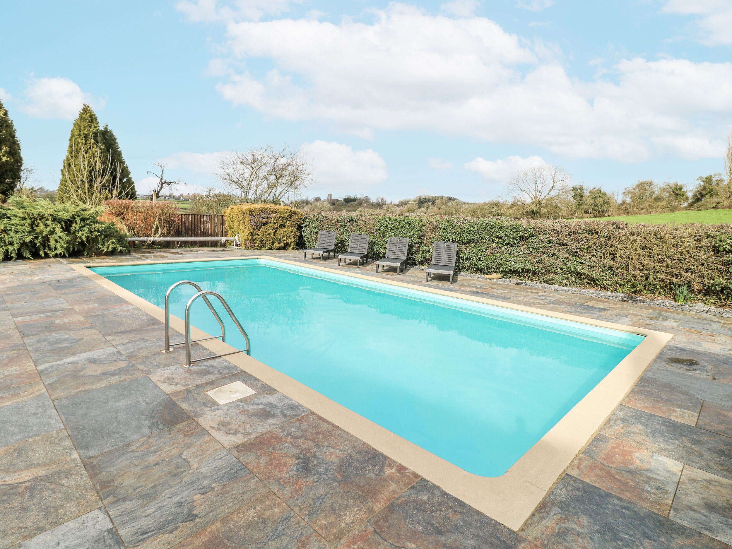 A rectangular swimming pool with a metal ladder on one side, surrounded by stone tiles.
