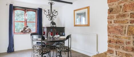 A dining area with a round table, zebra-striped chairs, a chandelier, and a view of the outdoors through a window.