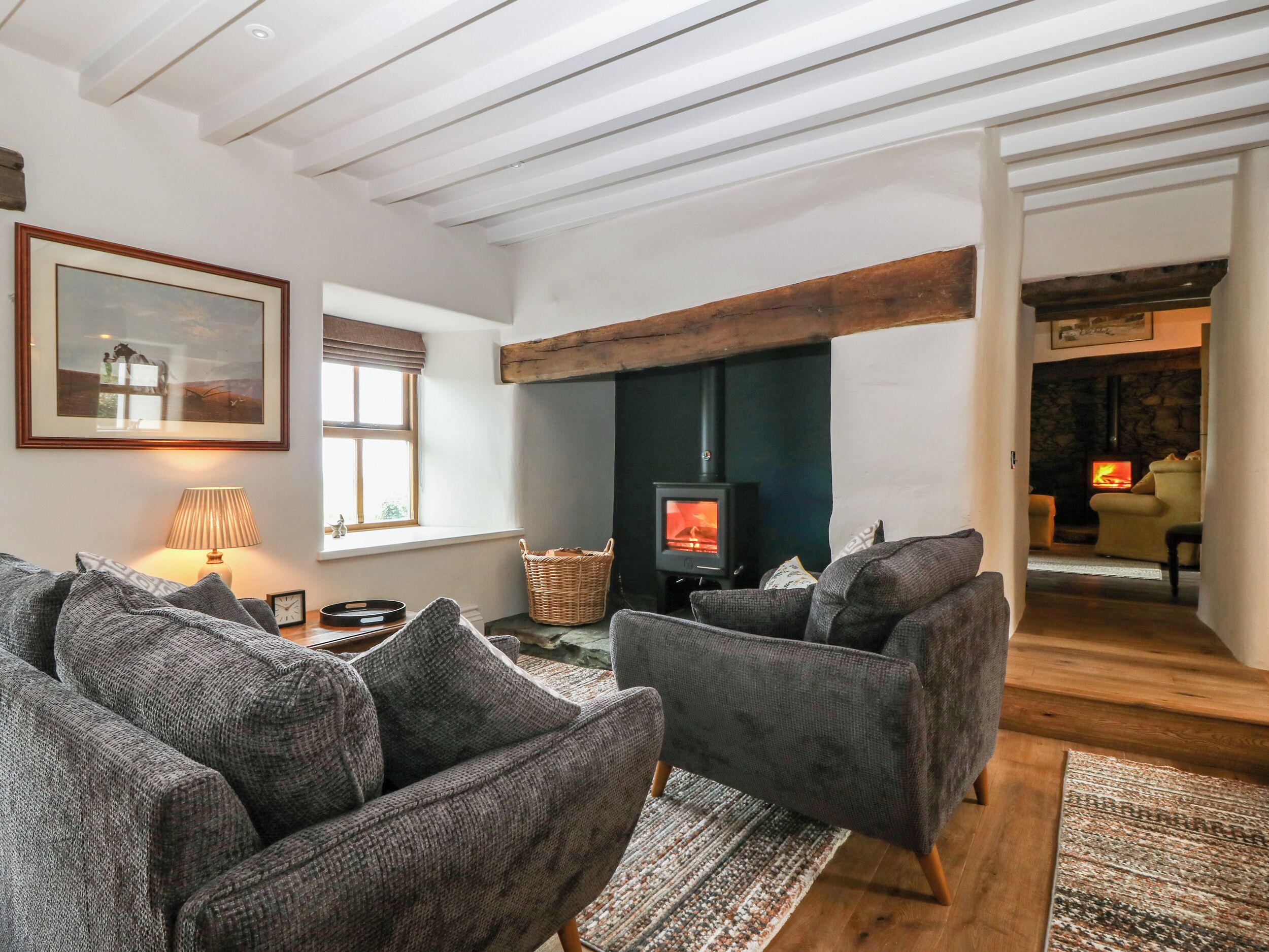 A cozy living room with a fireplace, grey sofas, a lamp, and a framed picture on the wall.