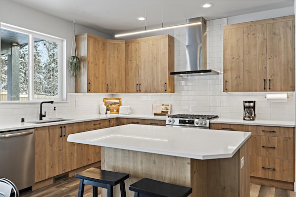 Una cocina moderna con armarios de madera, una isla grande, electrodomésticos de acero inoxidable y una ventana con vistas a árboles.
