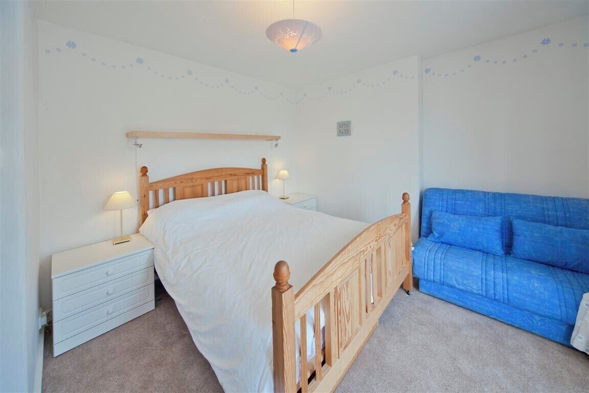 A bedroom with a wooden bed, white nightstands, a blue sofa, and a ceiling light fixture.