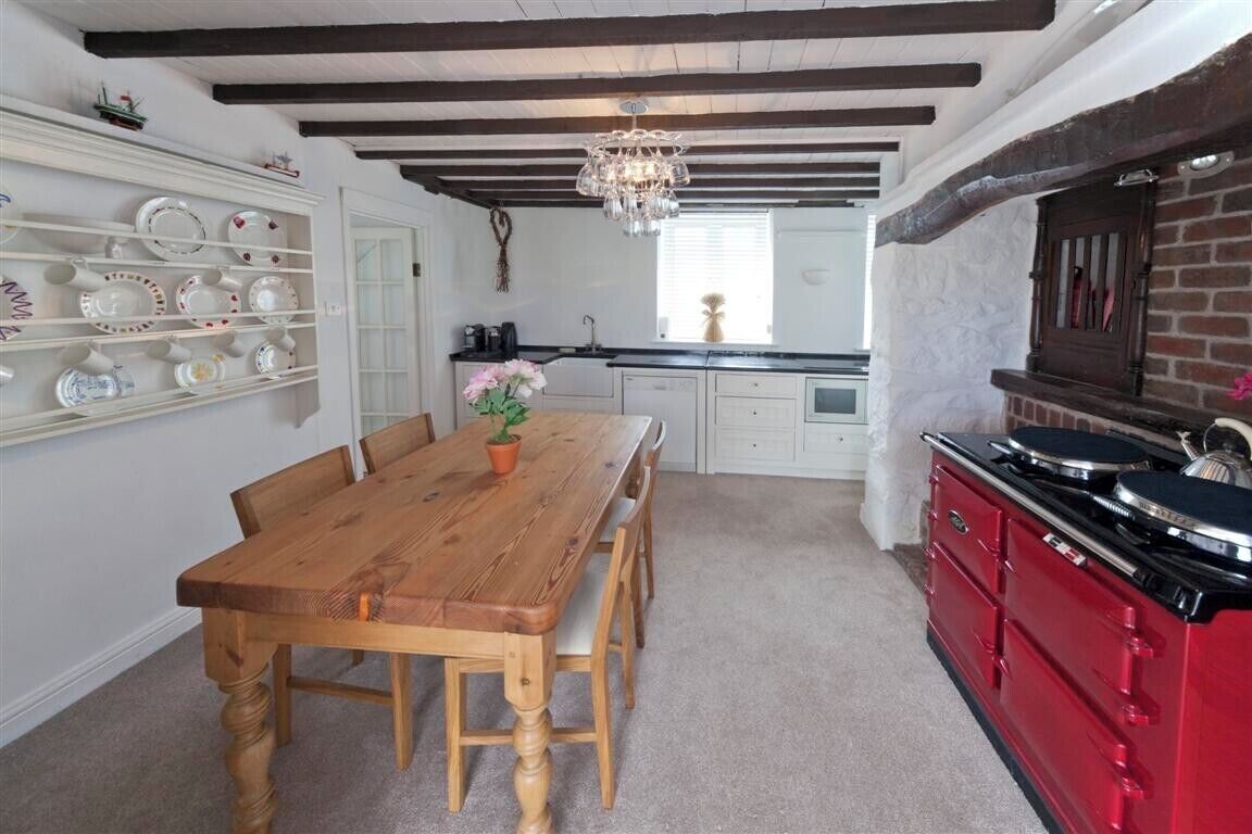 A kitchen with a wooden dining table, white cabinetry, and a red stove.