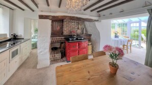 A rustic kitchen with exposed brick, a red stove, and a wooden table with a potted plant. - Ty Ffynnon (Pwllheli)