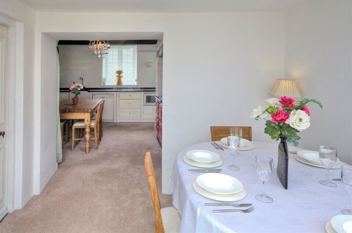 Un coin repas avec une table dressée pour quatre personnes, un vase rempli de fleurs et, au fond, une cuisine.
