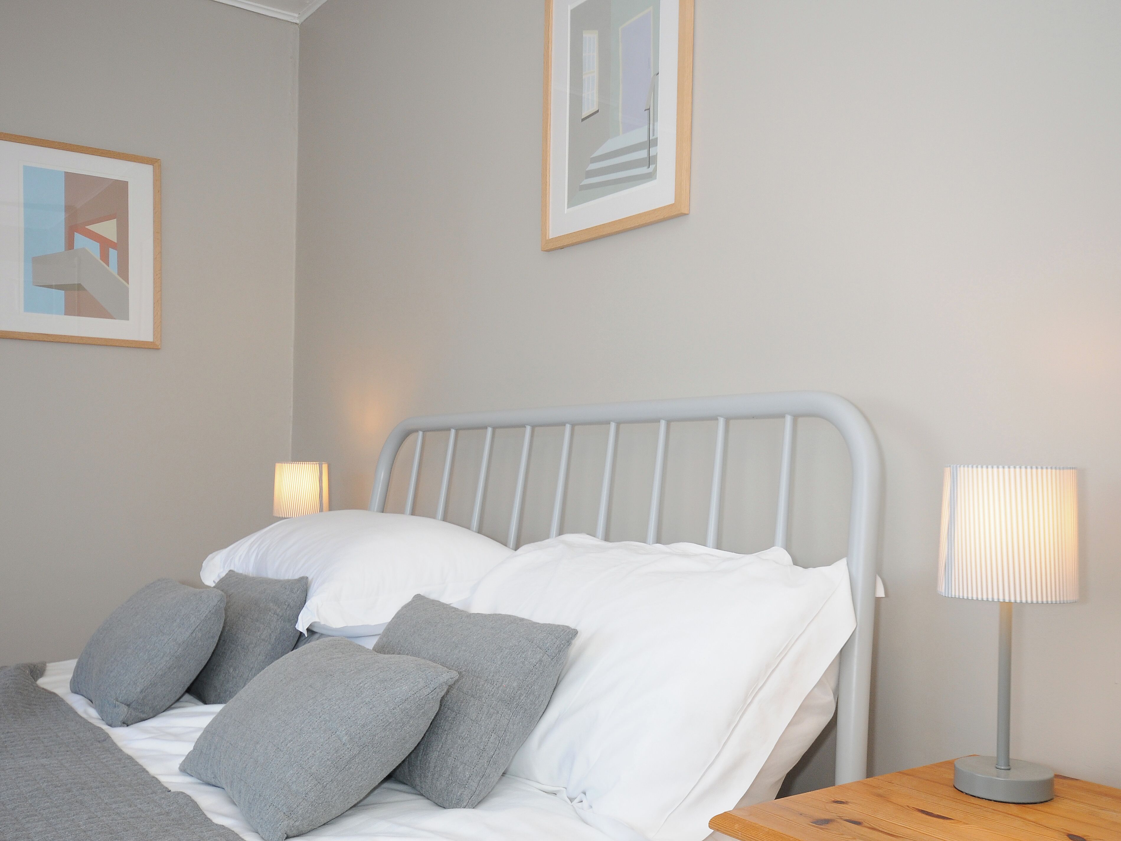 A neatly made bed with white and grey bedding, a grey metal headboard, and a bedside table with a lamp.