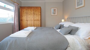 Une chambre à coucher avec un grand lit, une armoire, une fenêtre avec des rideaux et un tableau encadré au mur.