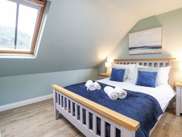 A neatly made bed with blue and white bedding, a wooden headboard, and two bedside lamps. - Tŷ Kinik (Llangollen)