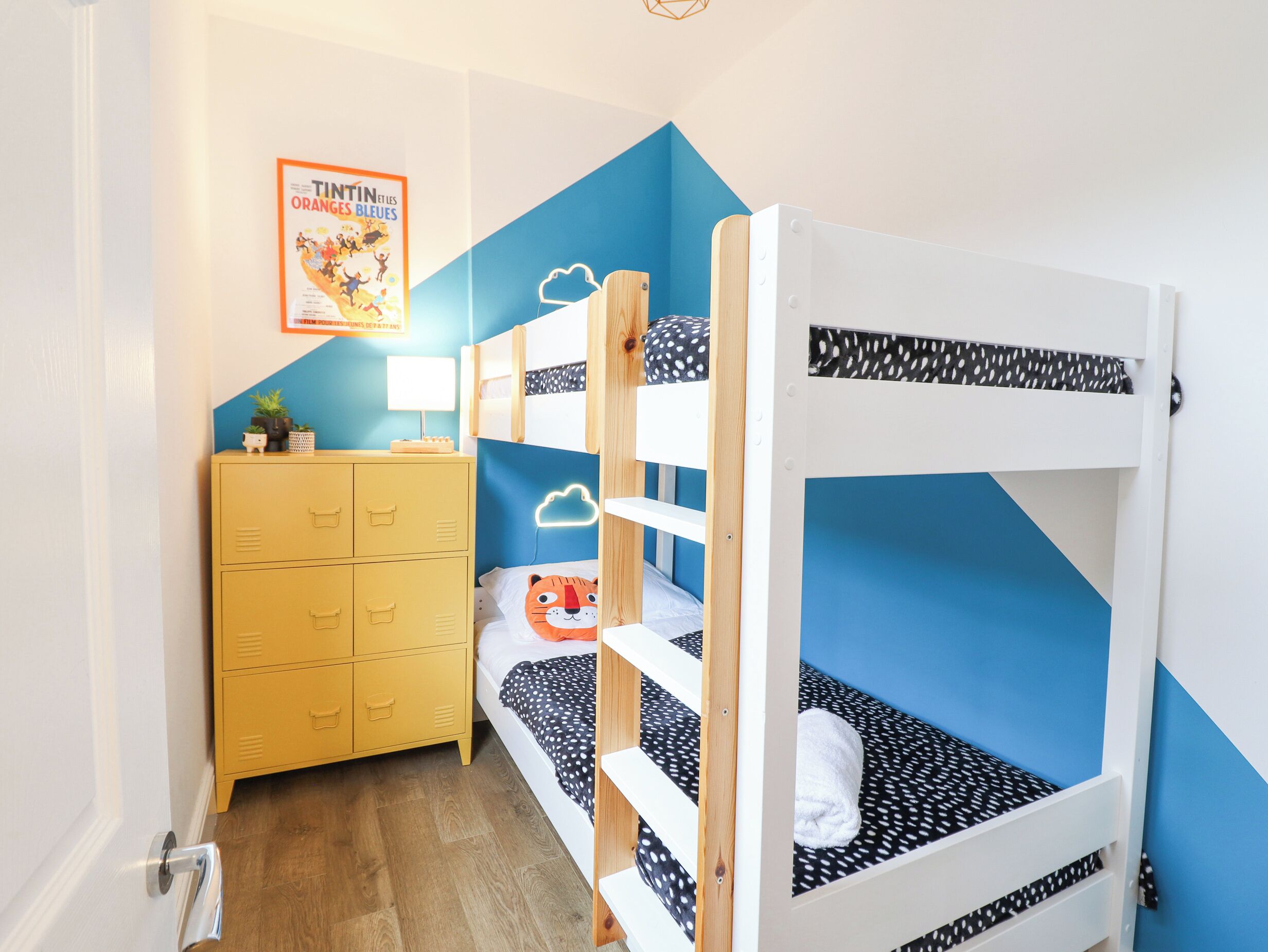 A bunk bed room with a blue accent wall, a yellow dresser, and a poster on the wall.
