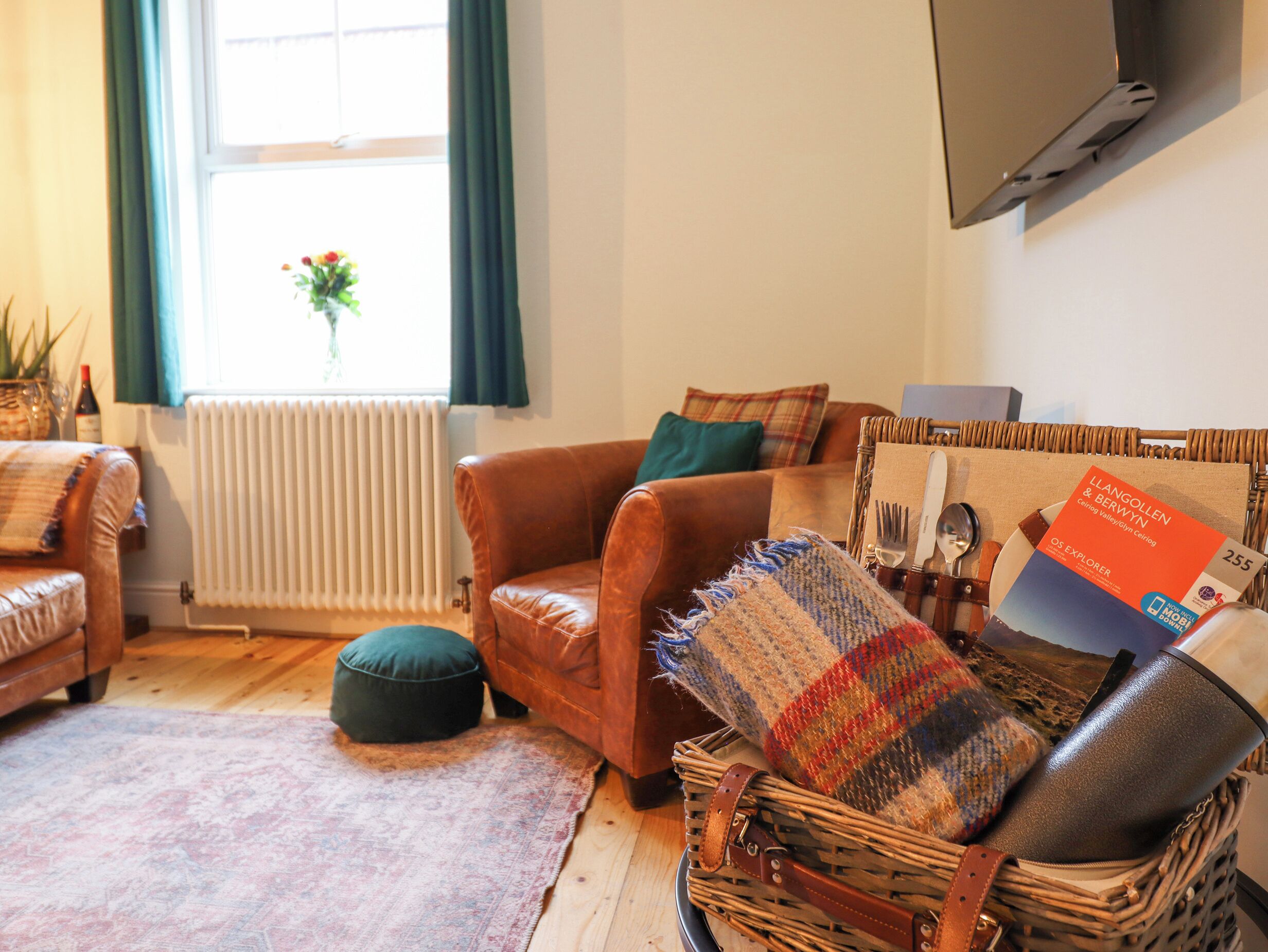 Een gezellige woonkamer met een bruine leren bank, een geweven mand met een plaid, en een eethoek bij een tafel.