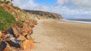 A coastal beach with a rocky shoreline, a staircase leading down to the beach, and a person walking in the distance.