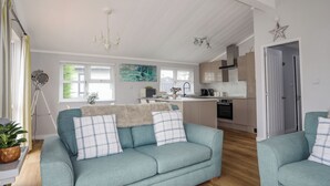 A spacious living room with a sofa and armchairs, a kitchen area with modern appliances, and a dining table.