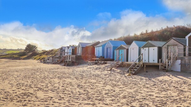 A row of beach huts with wooden stairs leading up to them, situated on a sandy beach.