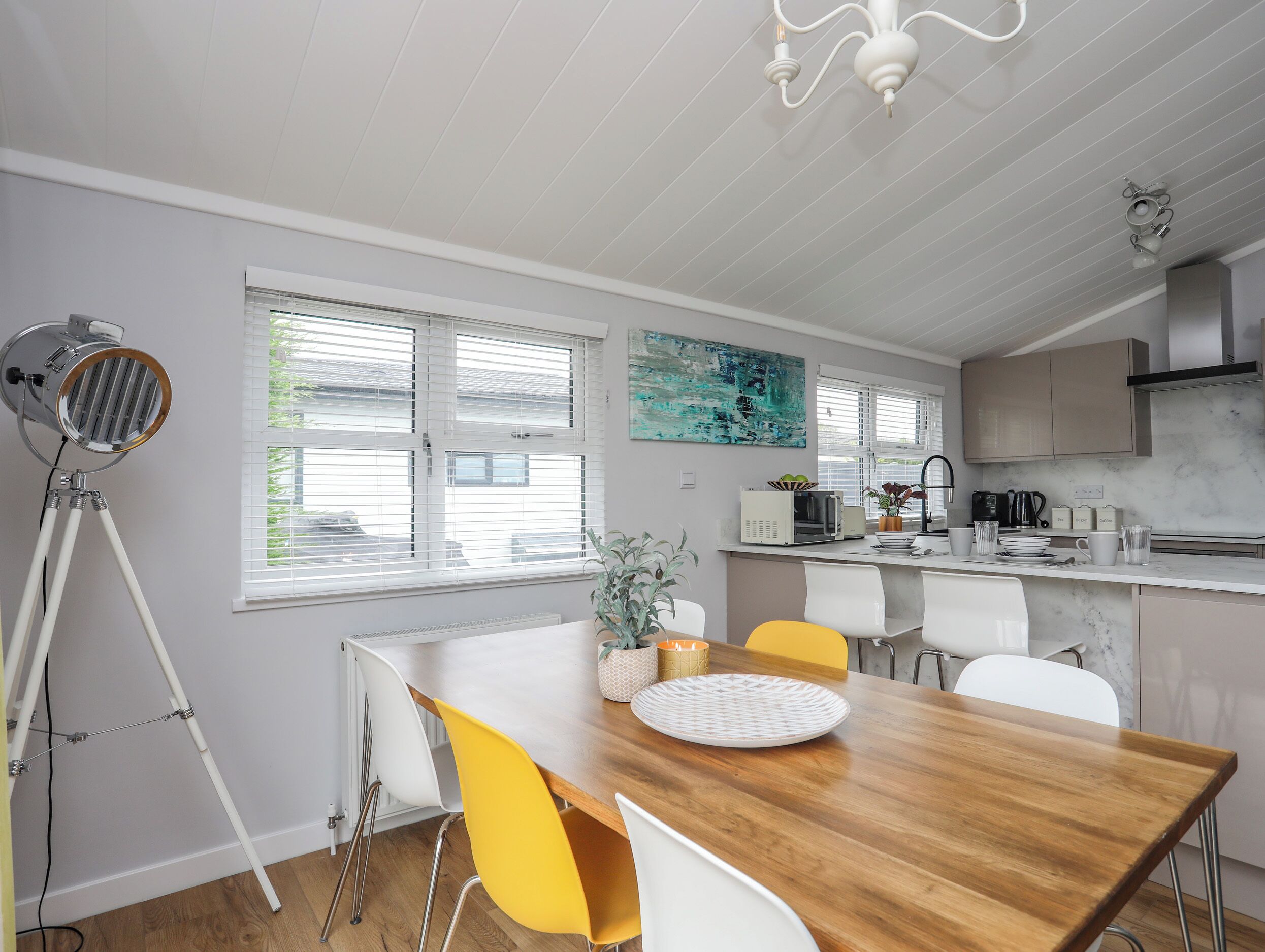 A modern kitchen with white cabinetry, a wooden dining table, and a tripod floor lamp.