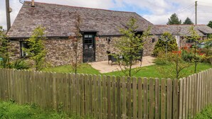 A stone cottage with a sloped roof, a wooden fence, and a small patio area with chairs. - Horseshoe Cottage (Bideford)