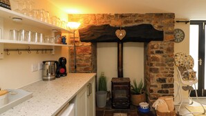 A kitchen with a stone fireplace, a coffee machine, and a baby high chair. - Horseshoe Cottage (Bideford)