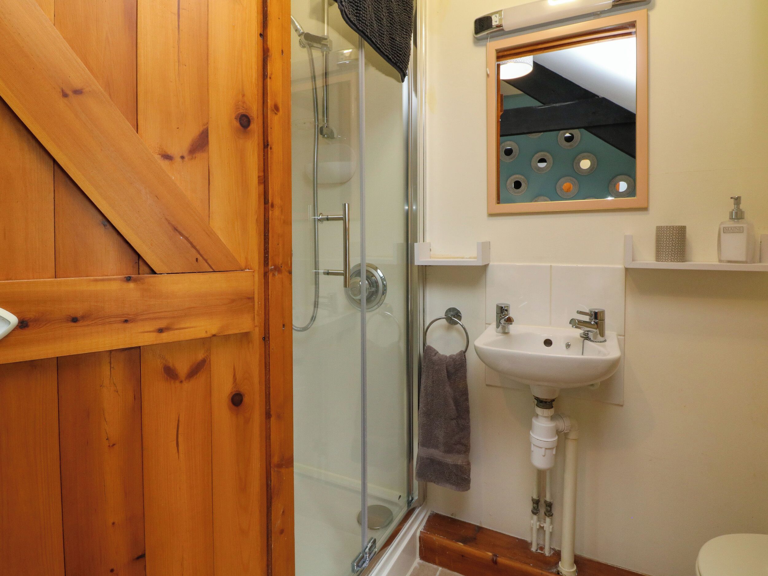 A bathroom with a wooden door, a glass shower enclosure, a sink, and a toilet.