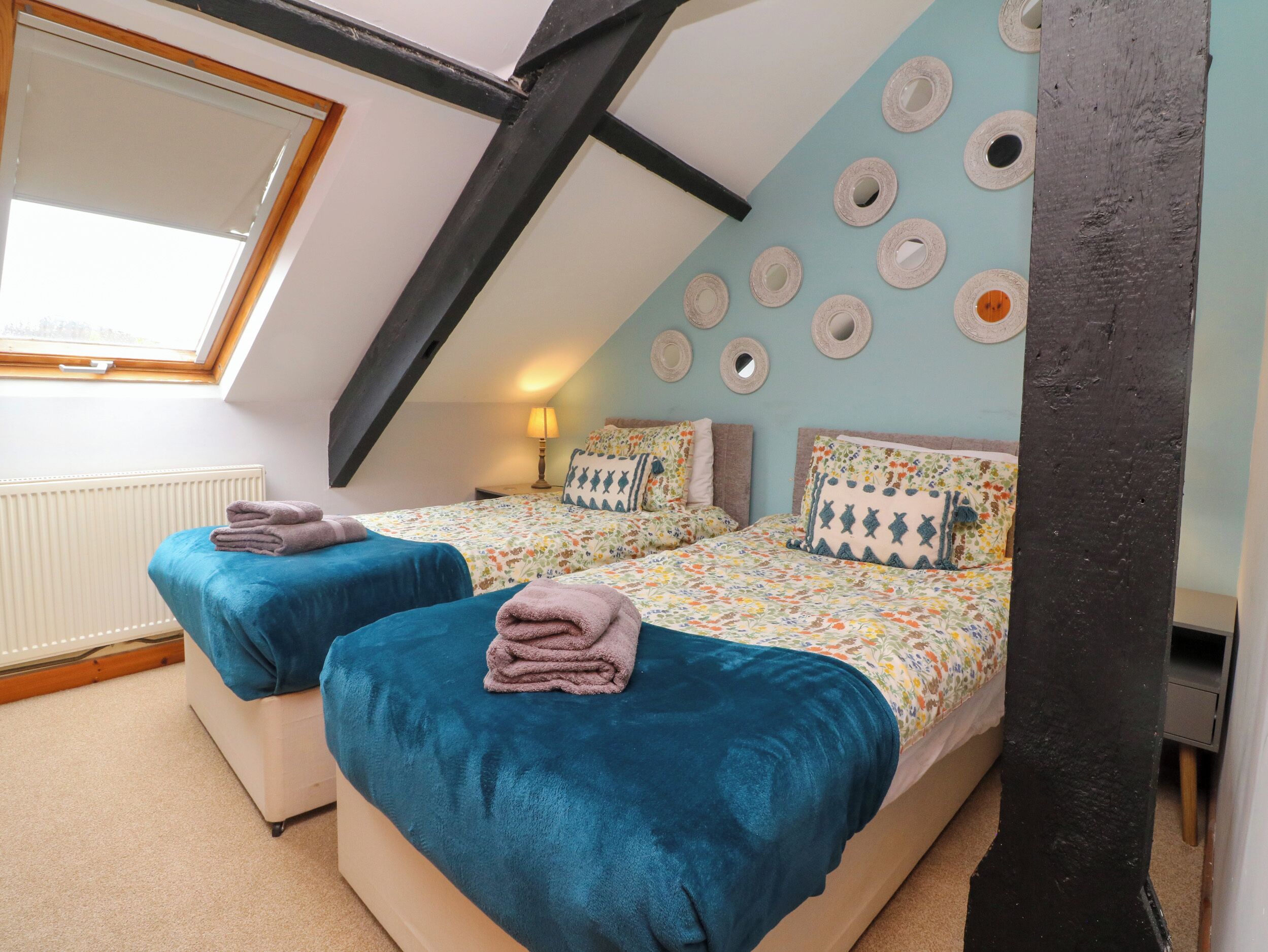 A cozy attic bedroom with two beds, a skylight, and a decorative wall with circular mirrors.