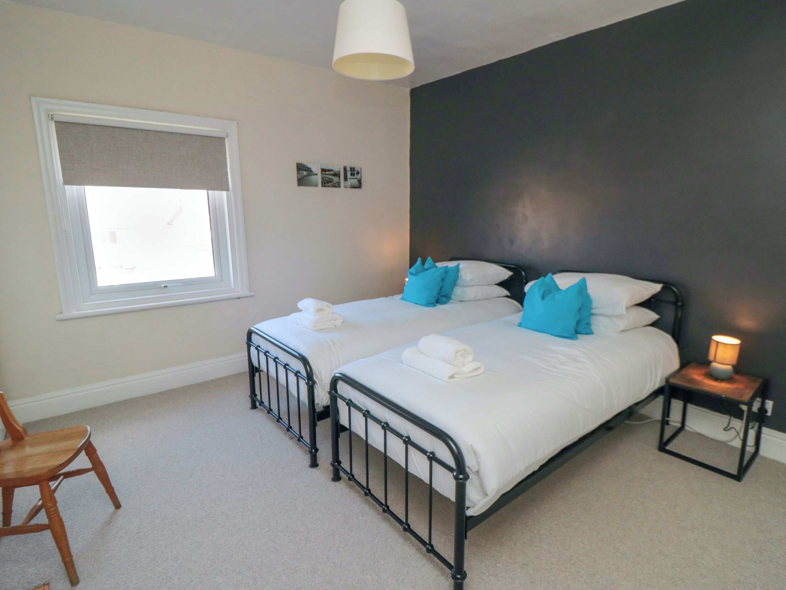 A bedroom with two beds, a window, a chair, and a nightstand with a lamp.