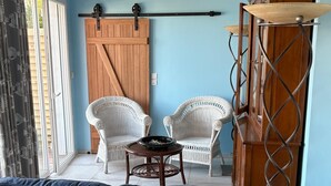 A living room with a blue sofa, two white wicker chairs, a wooden cabinet, and a metal spiral staircase. - La voile Bleue - A stopover with your feet in the water (Barbâtre)