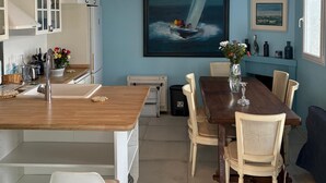 A modern kitchen with white cabinets, a wooden island, and a dining area with a wooden table and chairs. - La voile Bleue - A stopover with your feet in the water (Barbâtre)