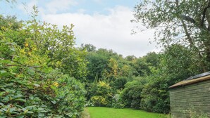 A lush garden with a wooden bench and a shed. - The Bothy (Bolton)
