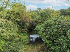 A garden with a table and chairs under a pergola surrounded by dense foliage. - The Bothy (Bolton)