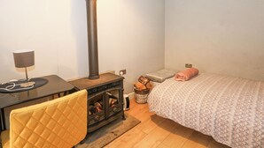 A cozy room with a bed, a chair, a table, a wall-mounted heater, and a small bedside table with a lamp. - The Bothy (Bolton)