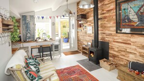 A cozy living room with a fireplace, wooden walls, and a dining area with a view to the garden.