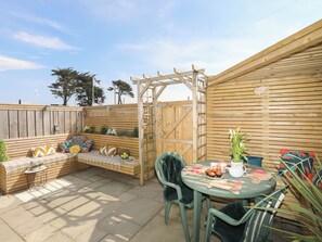 A patio with a wooden bench, a table with a teapot, and a gate. - Lle Te (Pwllheli)