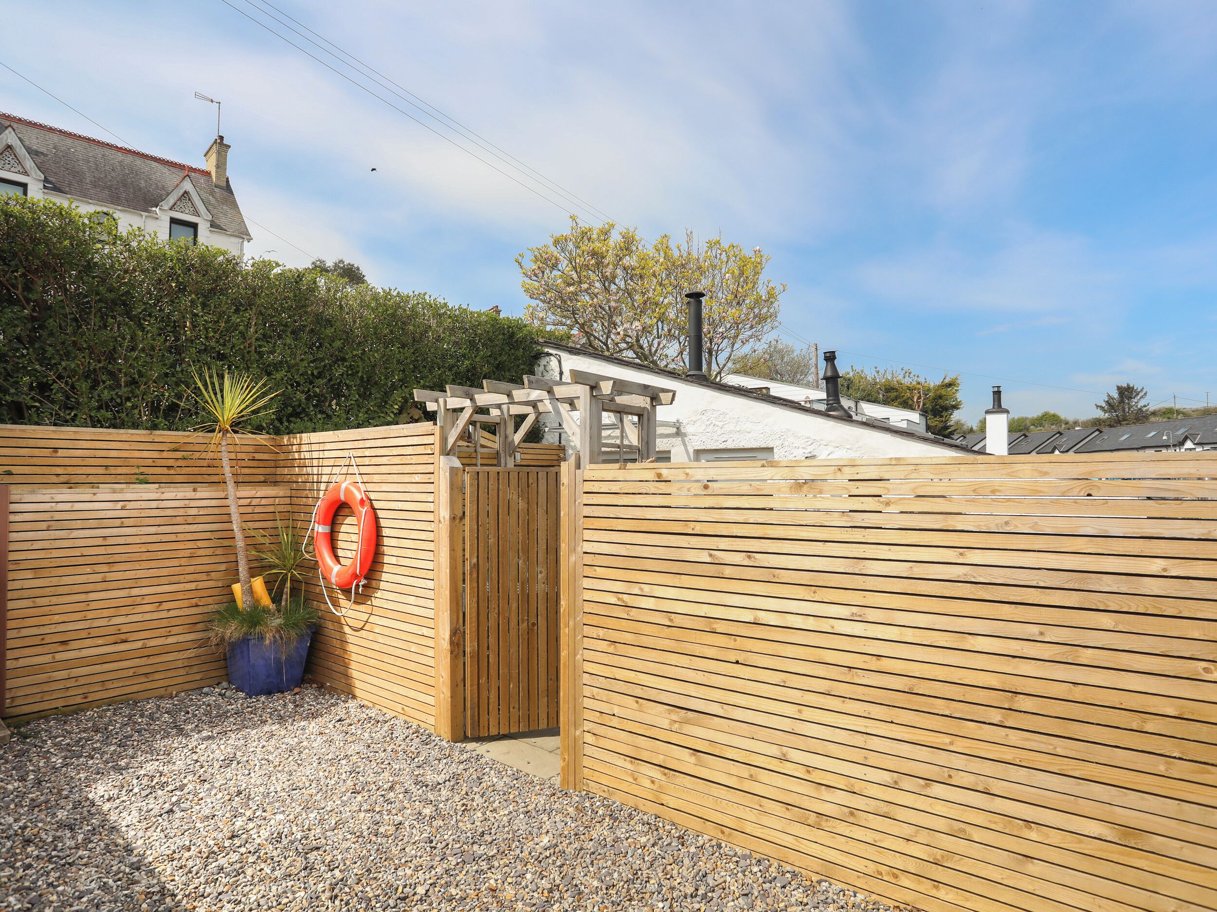 A wooden fence with a gate, a lifebuoy, and a small tree.