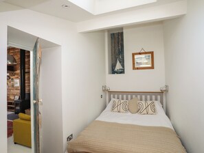 A bedroom with a bed, a headboard, a window with a view, and a door leading to another room. - Lle Te (Pwllheli)