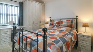 A bedroom with a bed, nightstands, a dresser, and a window with curtains. - Tyddyn Bach (Holyhead)