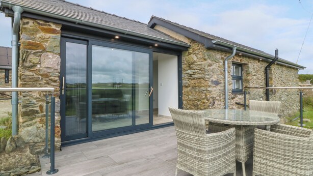 A stone building with a glass door and a patio area with wicker furniture. - Tyddyn Bach (Holyhead)