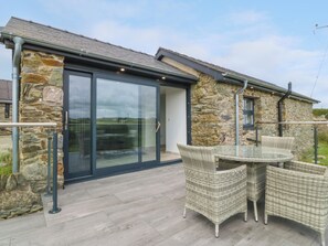 A stone building with a glass door and a patio area with wicker furniture. - Tyddyn Bach (Holyhead)