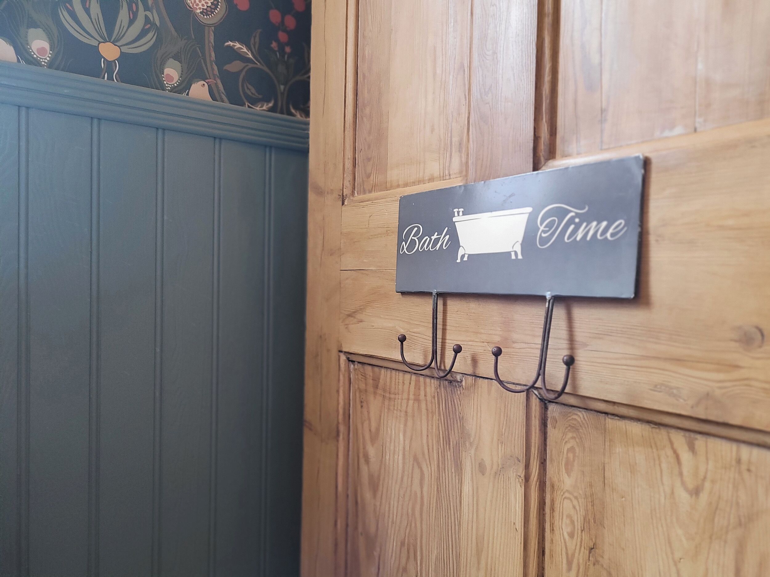 A wooden wall with a sign that reads "Bath Time" and a hook for hanging items.